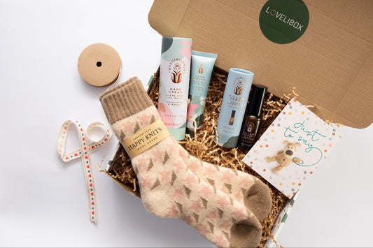 Gift box with a pair of socks, cream, and other items on a white background